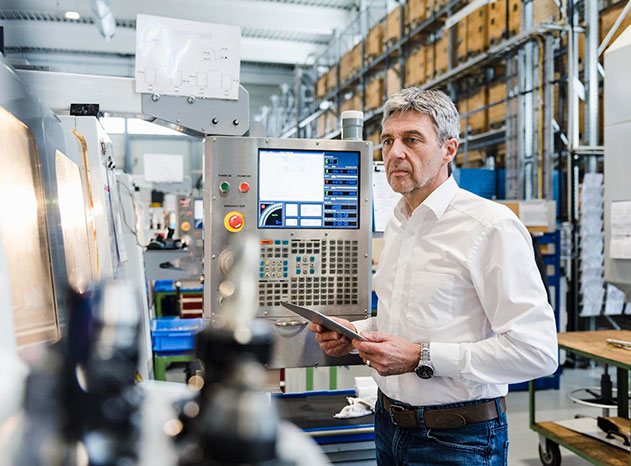 Hombre con tablet observa el panel de control de una máquina industrial en una nave
